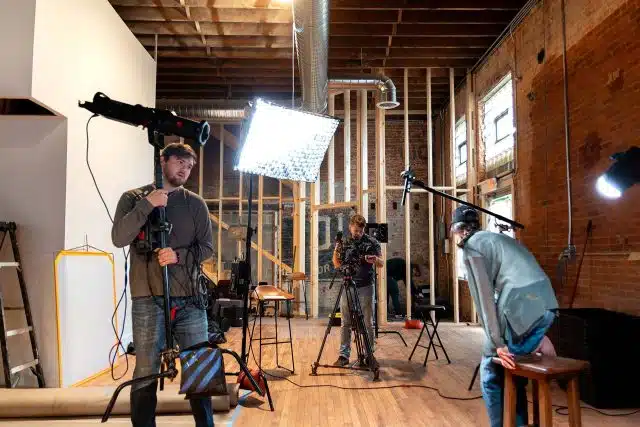 Three DreamOn Studios staff members working to set up a training video shoot in a room with exposed wooden beams.